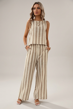 Ensemble femme à rayures beige et crème, haut sans manches et pantalon large, sur fond studio retouché par IA.
